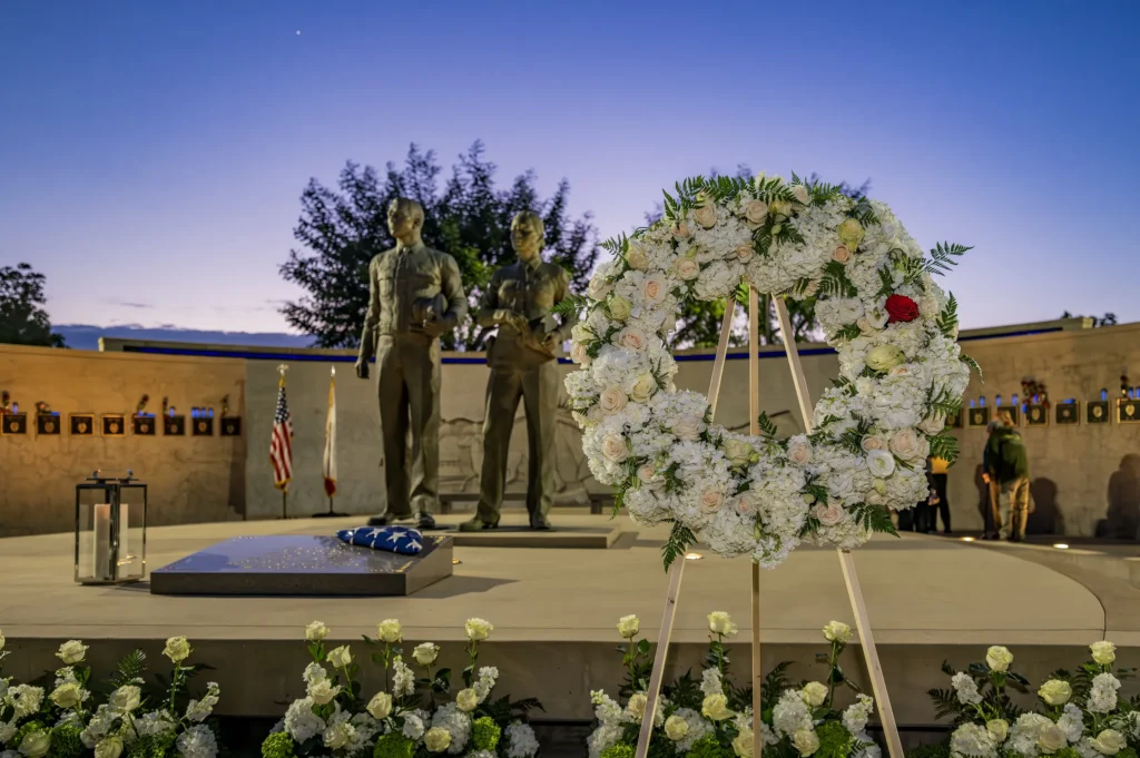 White flower wreath in front of the Peace Officers’ Memorial statues at dusk, 2026 ceremony